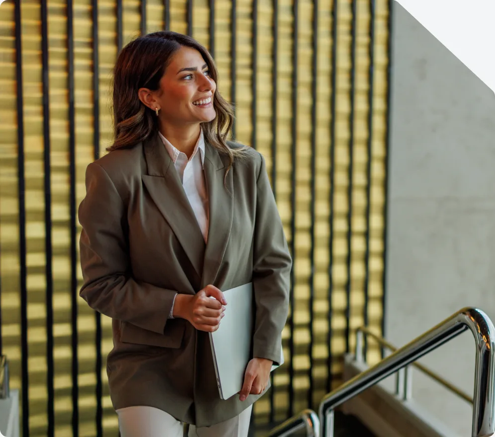 A professional in a blazer carrying a laptop on a staircase in an office lobby