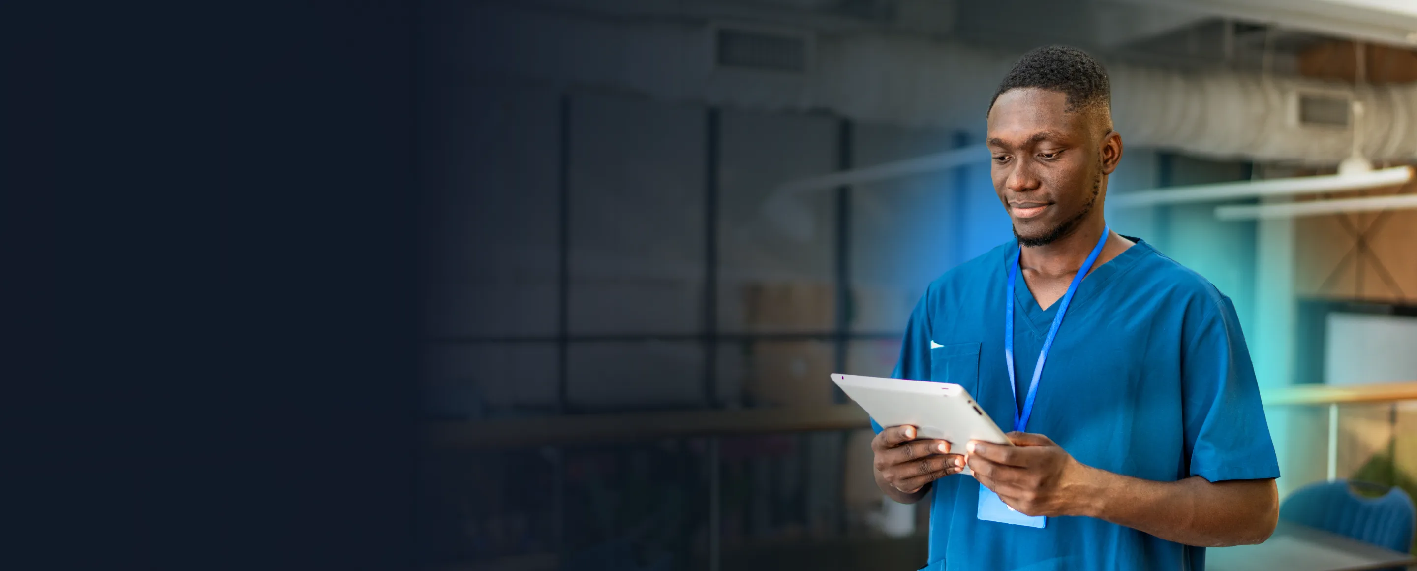 A nurse in scrubs reading a tablet on a hospital walkway