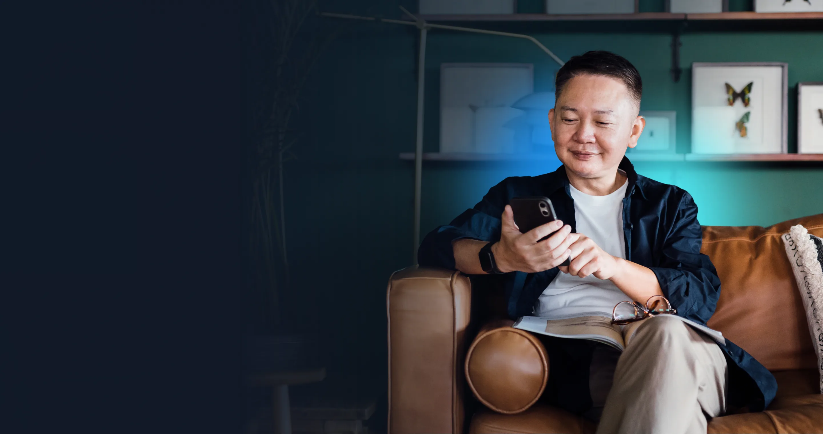 A man sitting in an armchair at home, looking at his phone