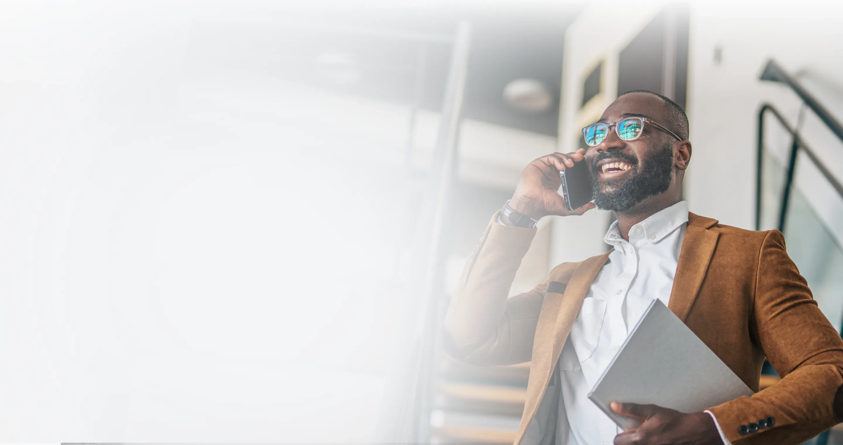 A man in a jacket smiling as he takes a call on his phone while walking down an office staircase