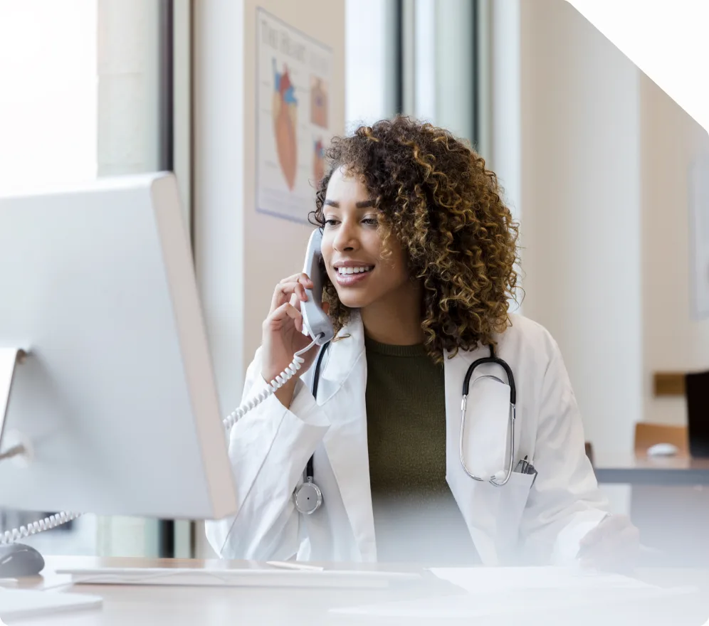 A clinician in a white coat on the phone at a workstation