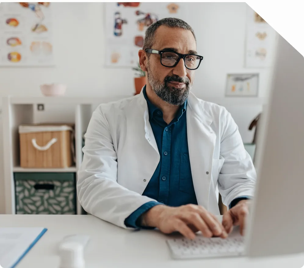 A physician in a white coat working at a desktop computer in a consulting room
