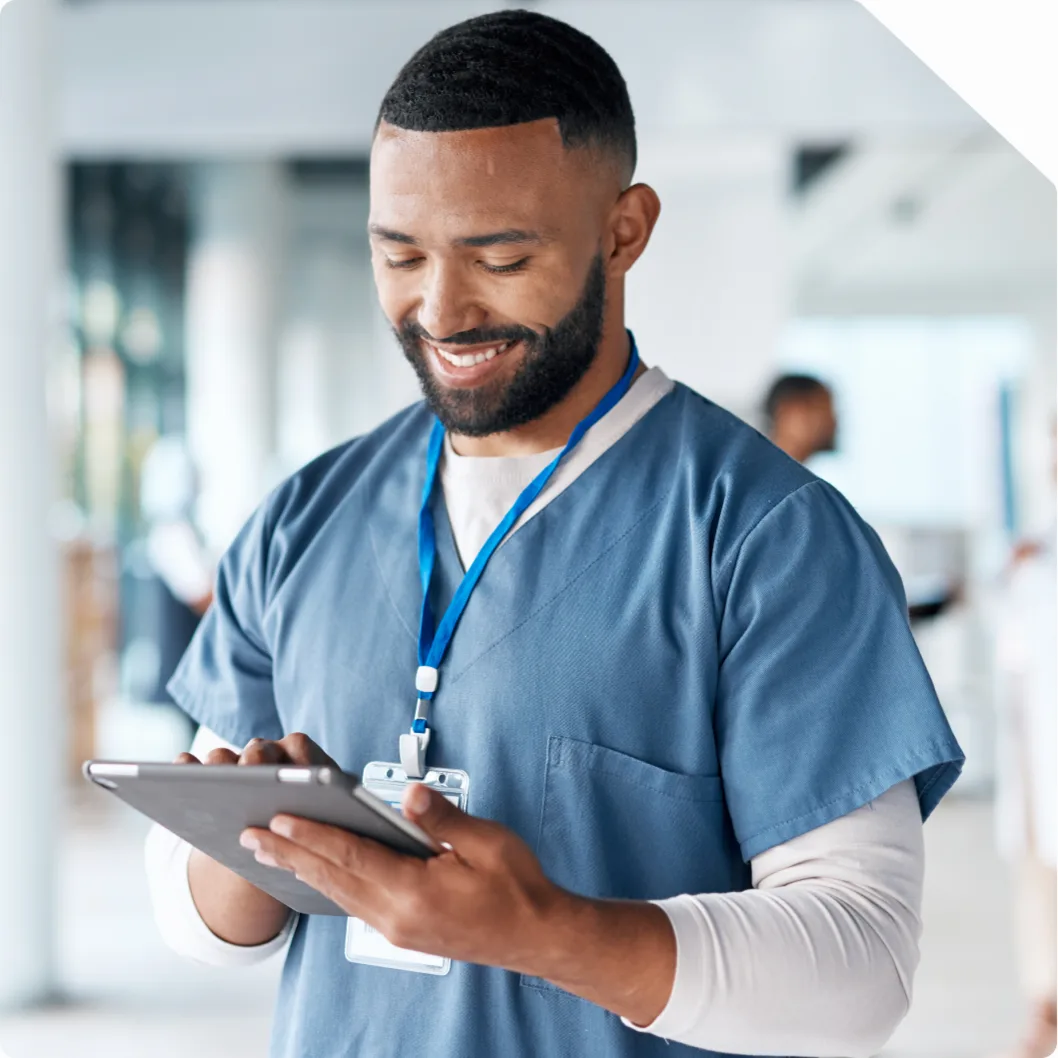 A nurse in scrubs smiling while reading a tablet on a hospital ward