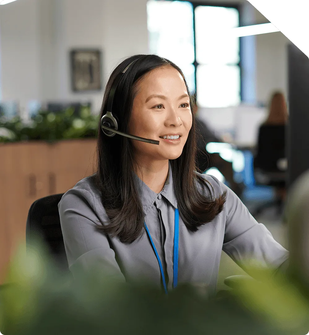 A support agent wearing a headset smiling at her screen in an open-plan office