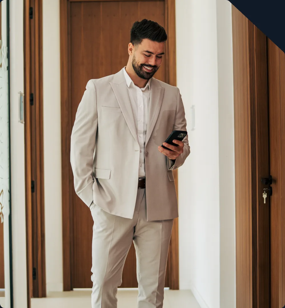 A man in a light suit reading his phone while walking down an office corridor