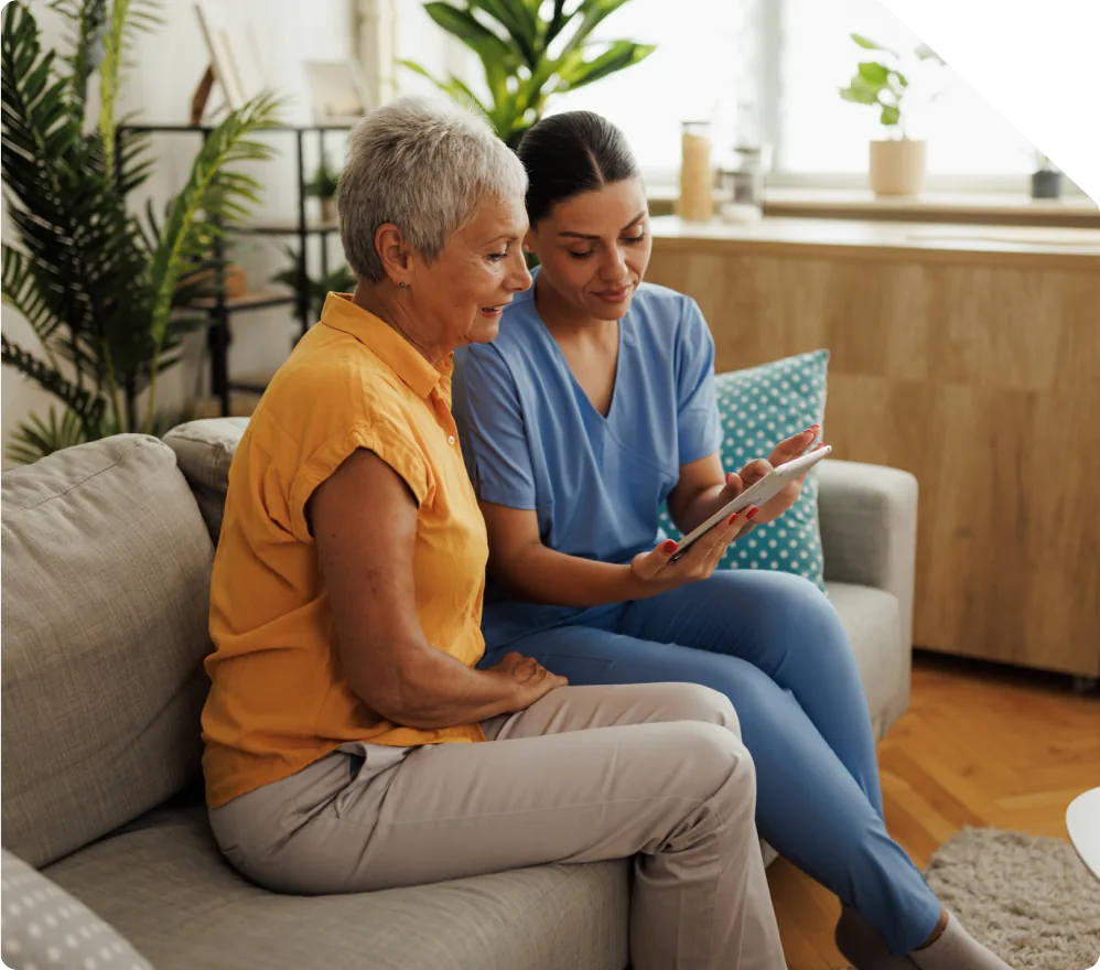 Two women sitting together on a sofa looking at a tablet