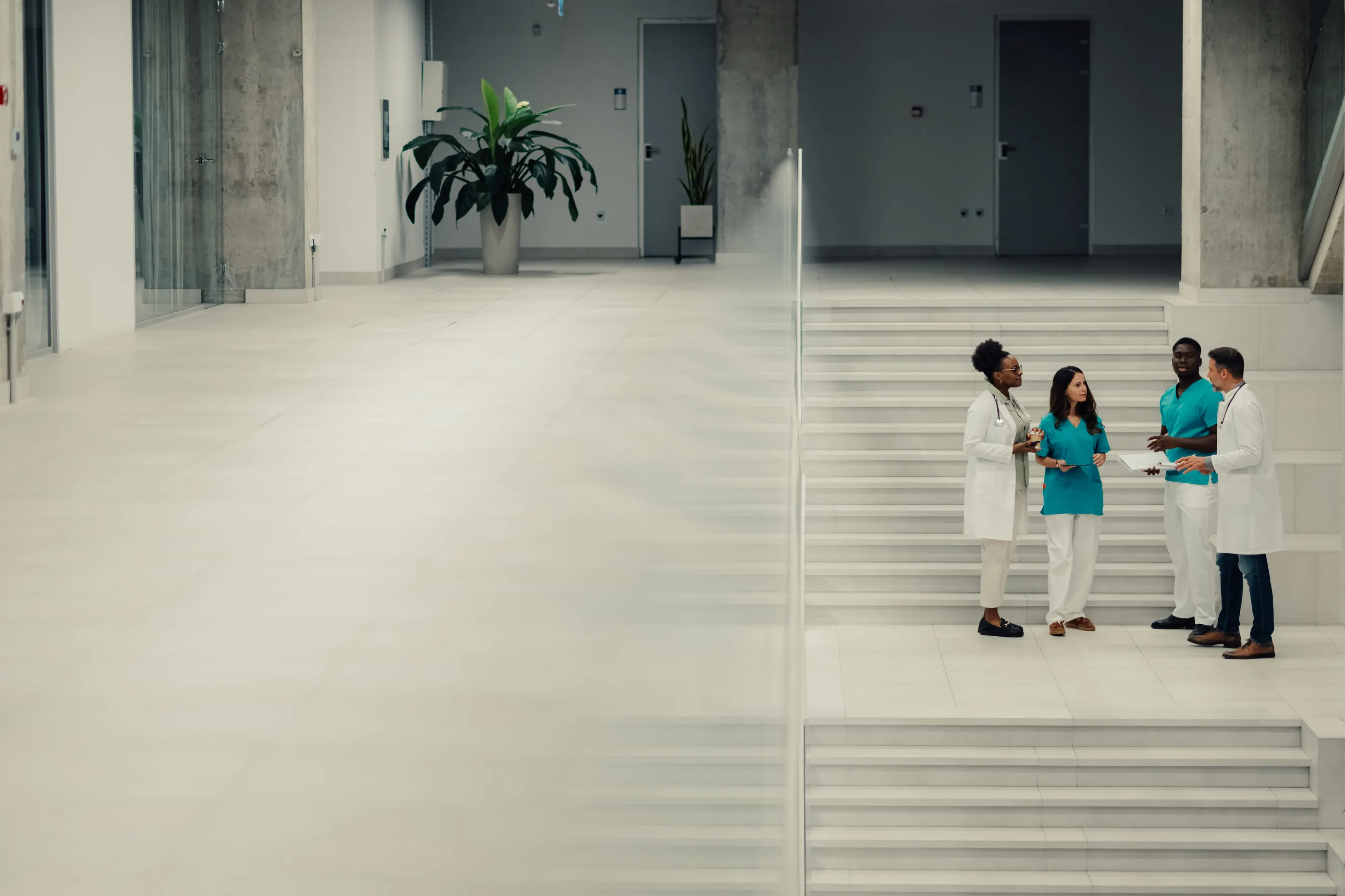 Four clinicians in conversation on the steps of a bright hospital atrium