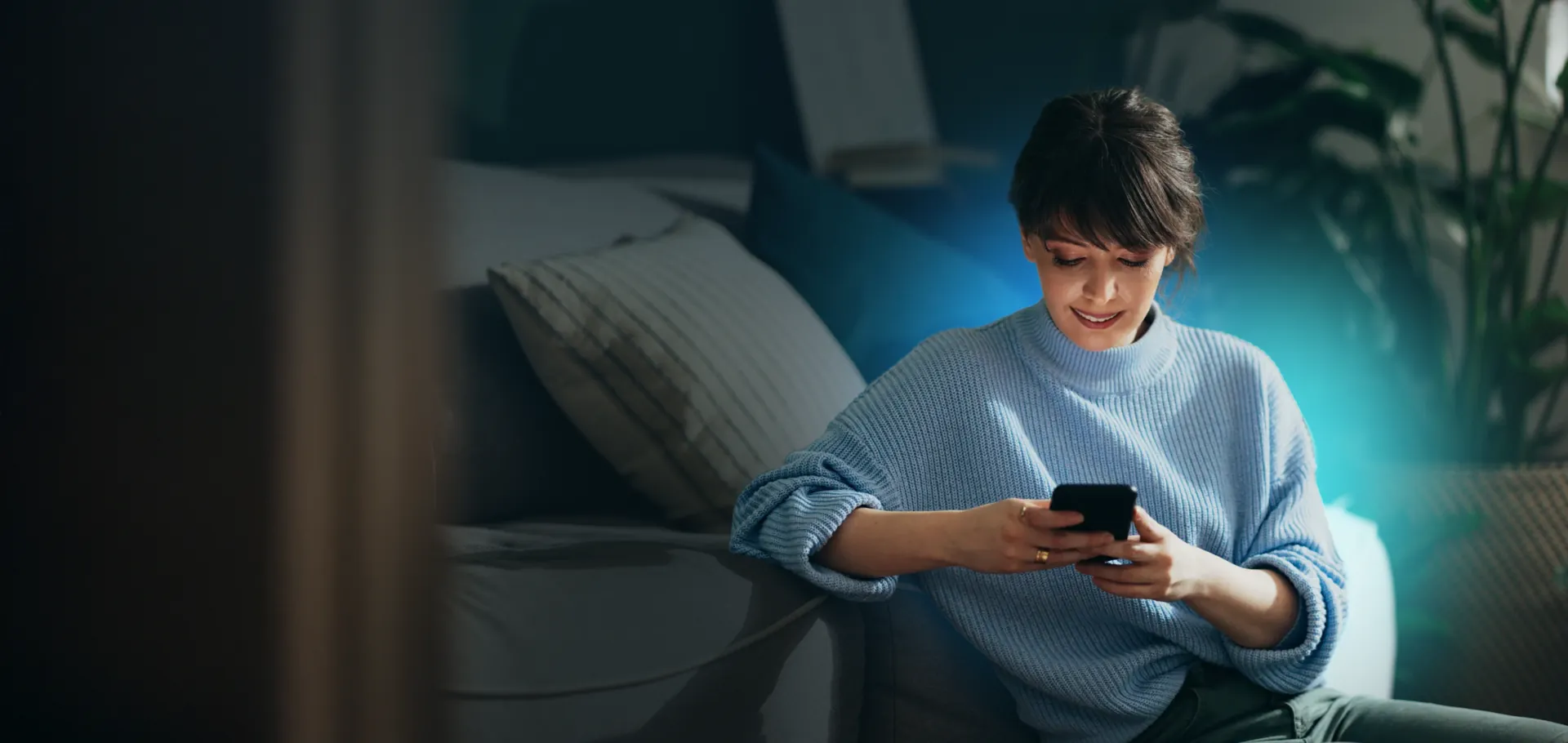 A woman sitting on a sofa at home, reading something on her phone