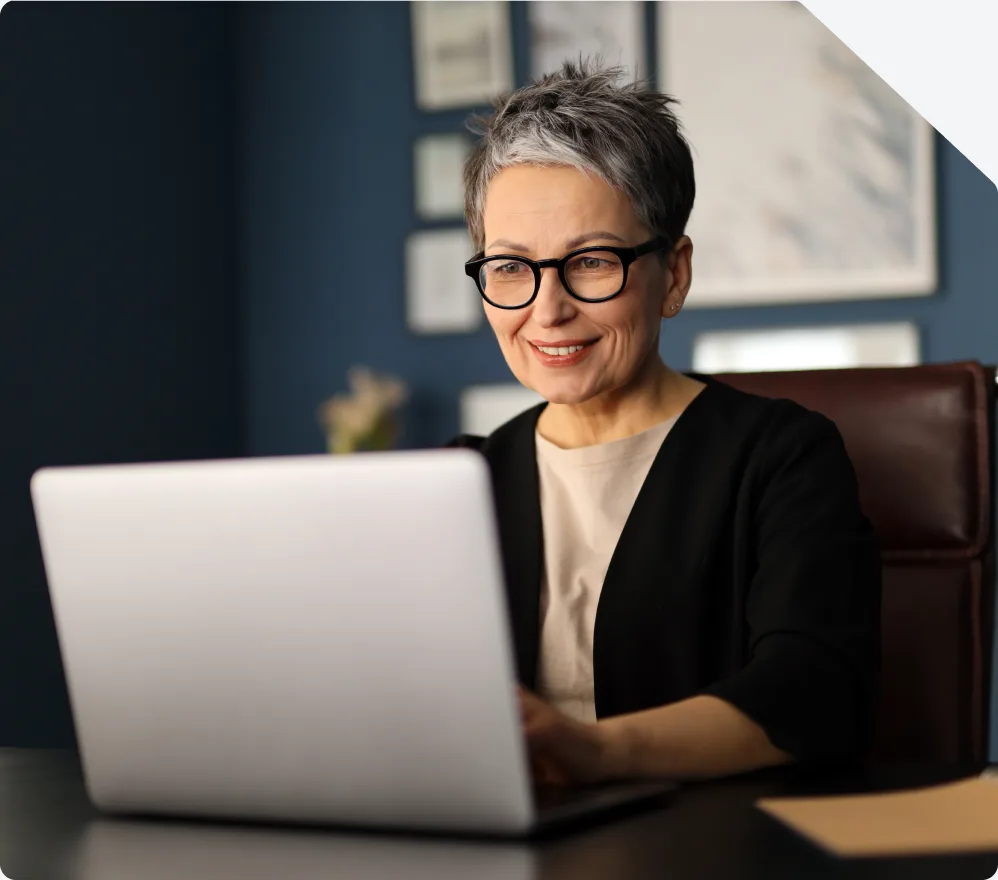 An older member smiling while catching up on her health plan messages at a laptop