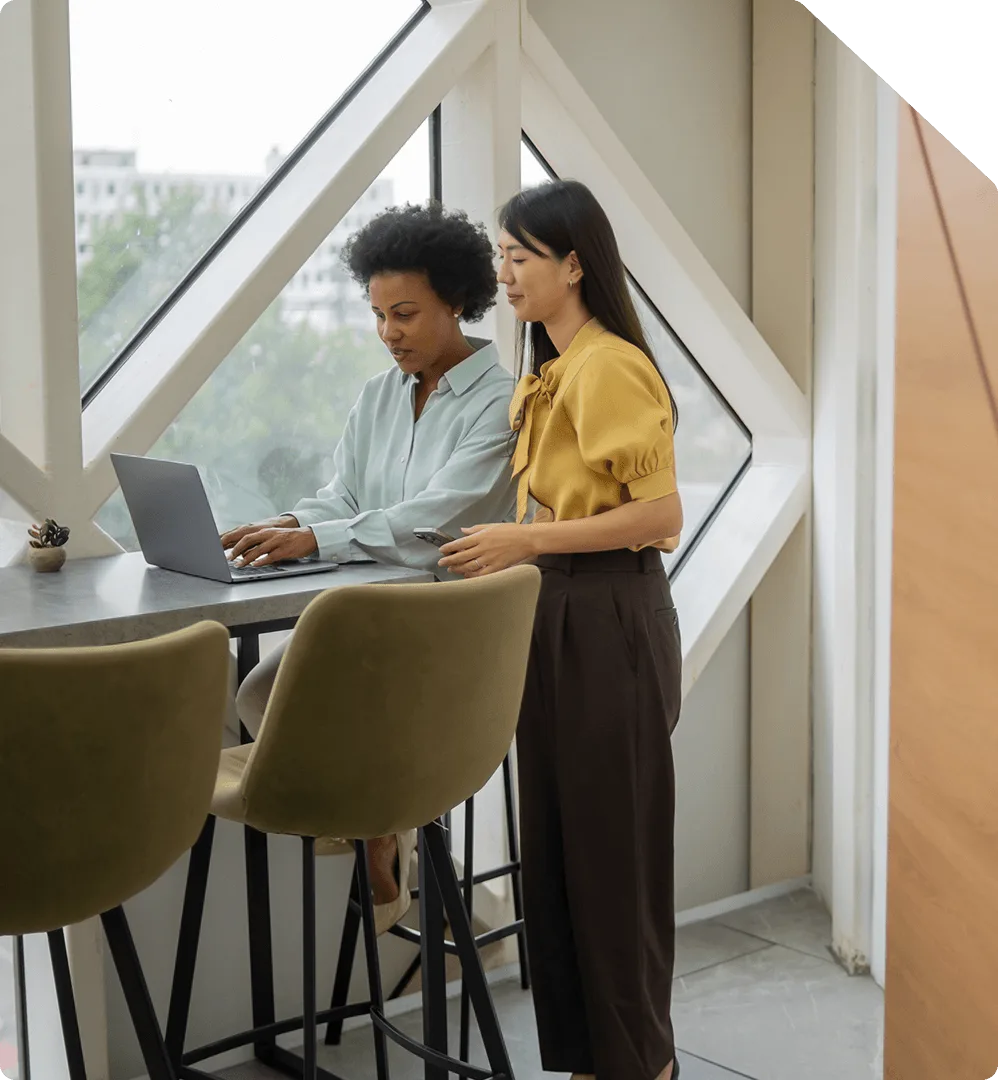 Two colleagues reviewing coverage details together on a laptop by an office window