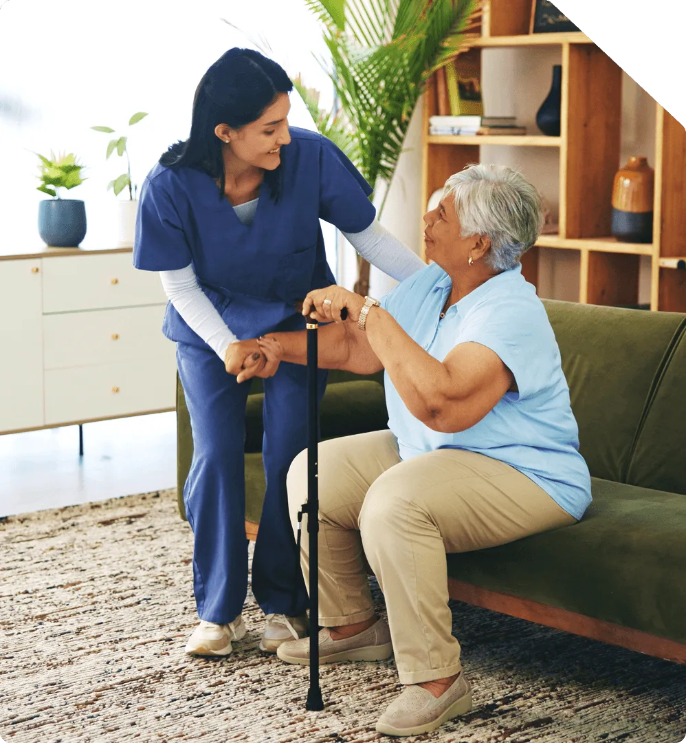 A nurse steadying a patient with a walking cane as she rises from a sofa at home