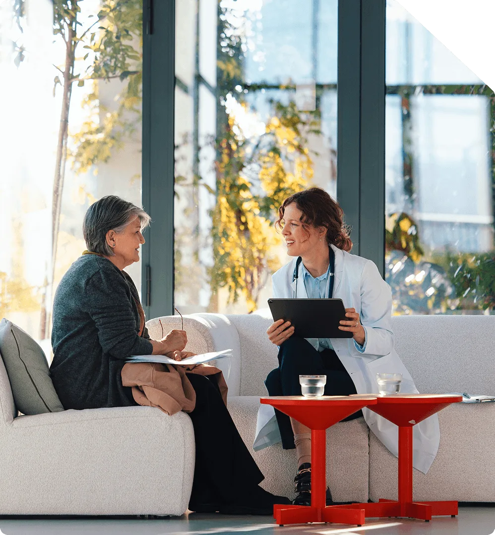 A clinician with a tablet reviewing paperwork with a patient in a bright waiting area
