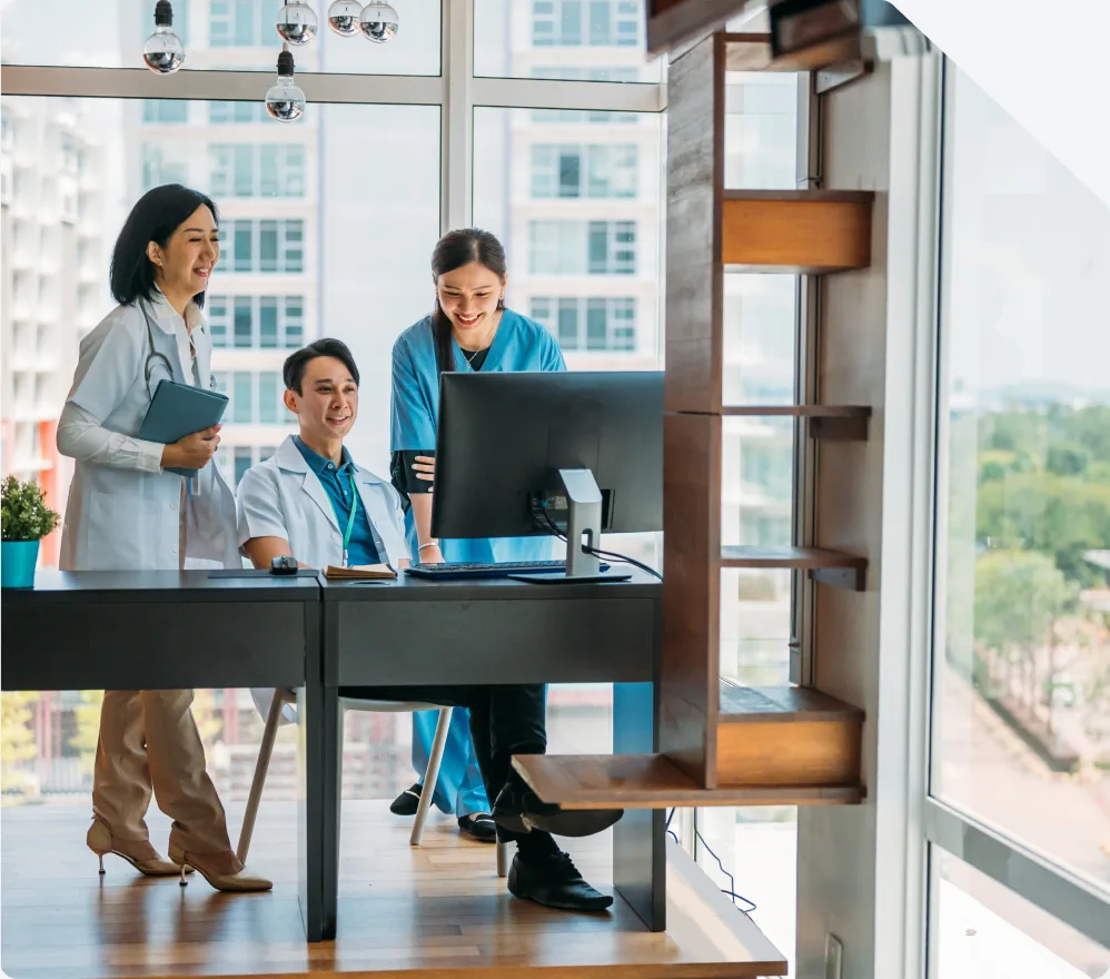 Three clinicians reviewing a screen at a desk by a window