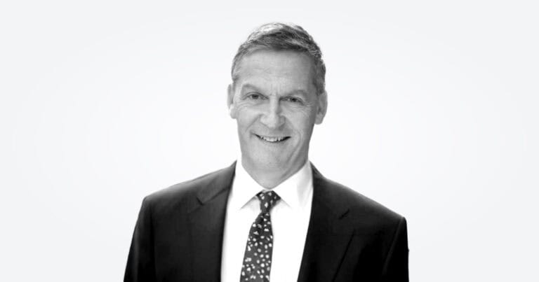 A black-and-white photograph of new board member John Driscoll wearing a jacket and tie.